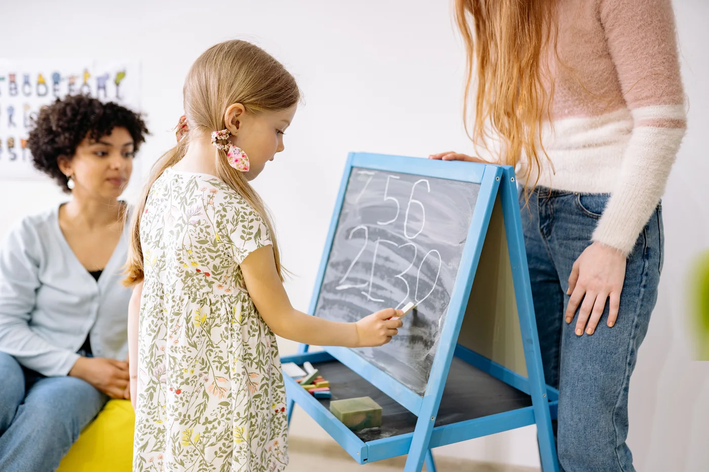 A child writing on a classroom board with adults nearby